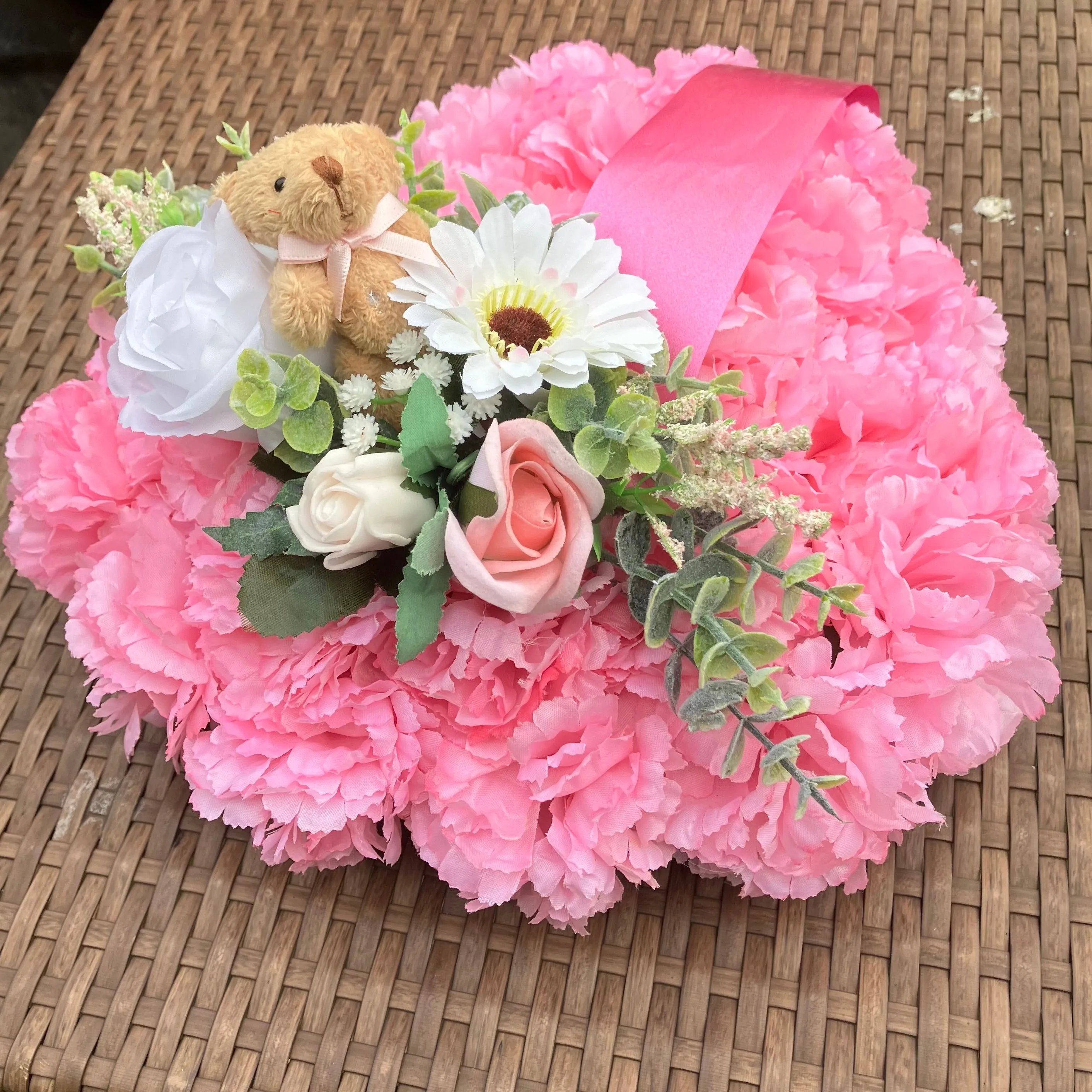 a memorial heart of artificial silk roses and carnations in shades of pink