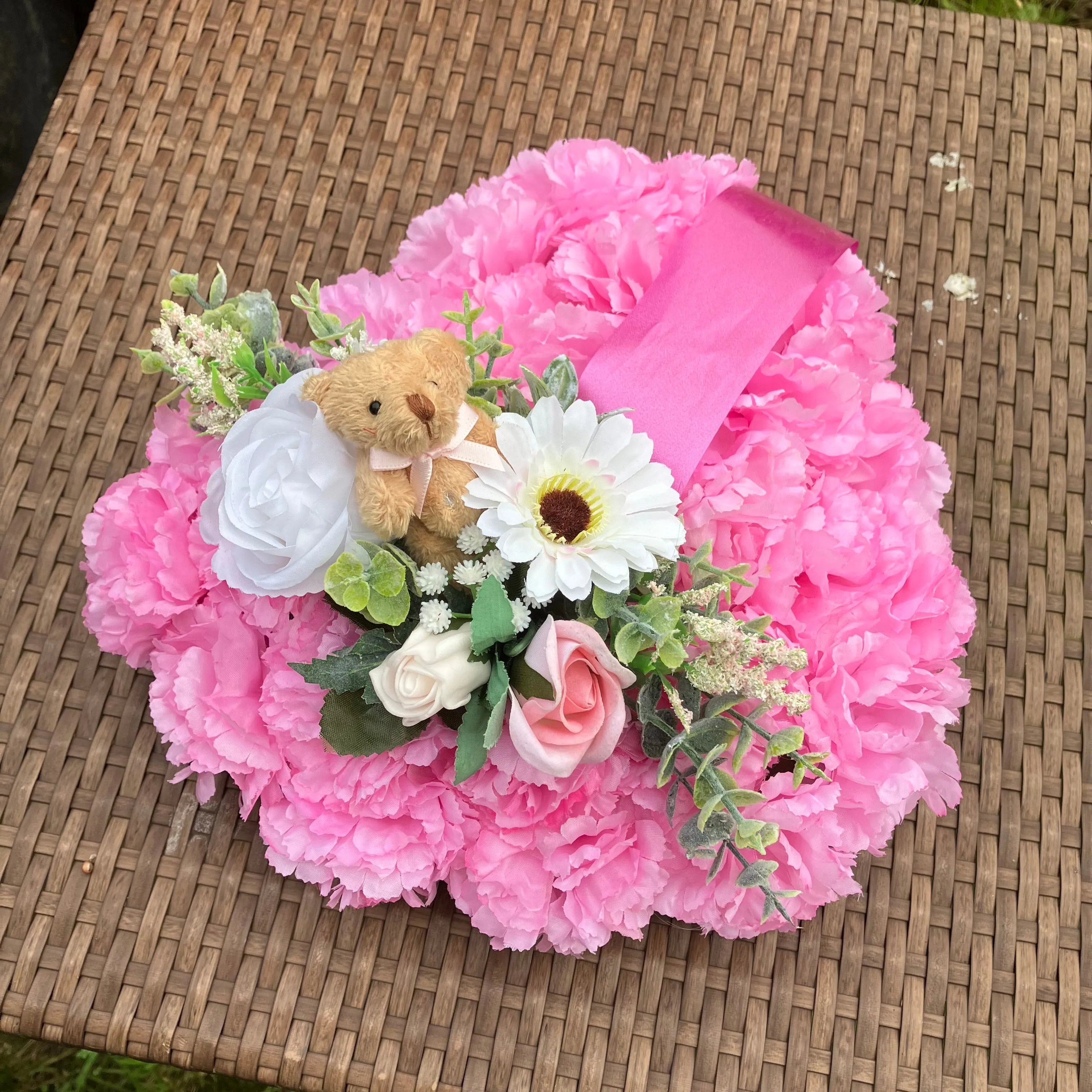 a memorial heart of artificial silk roses and carnations in shades of pink