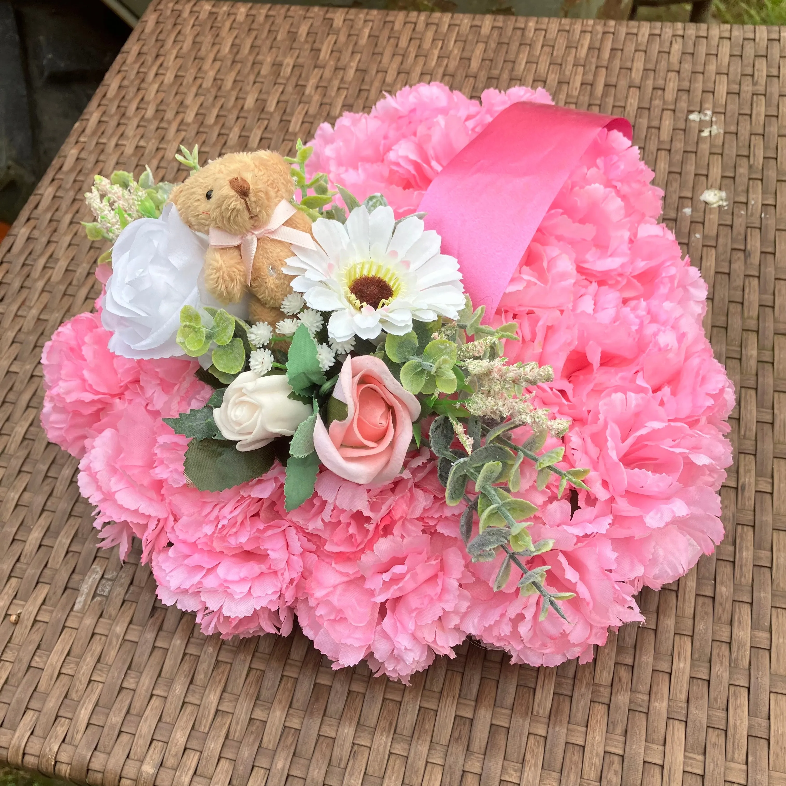 a memorial heart of artificial silk roses and carnations in shades of pink